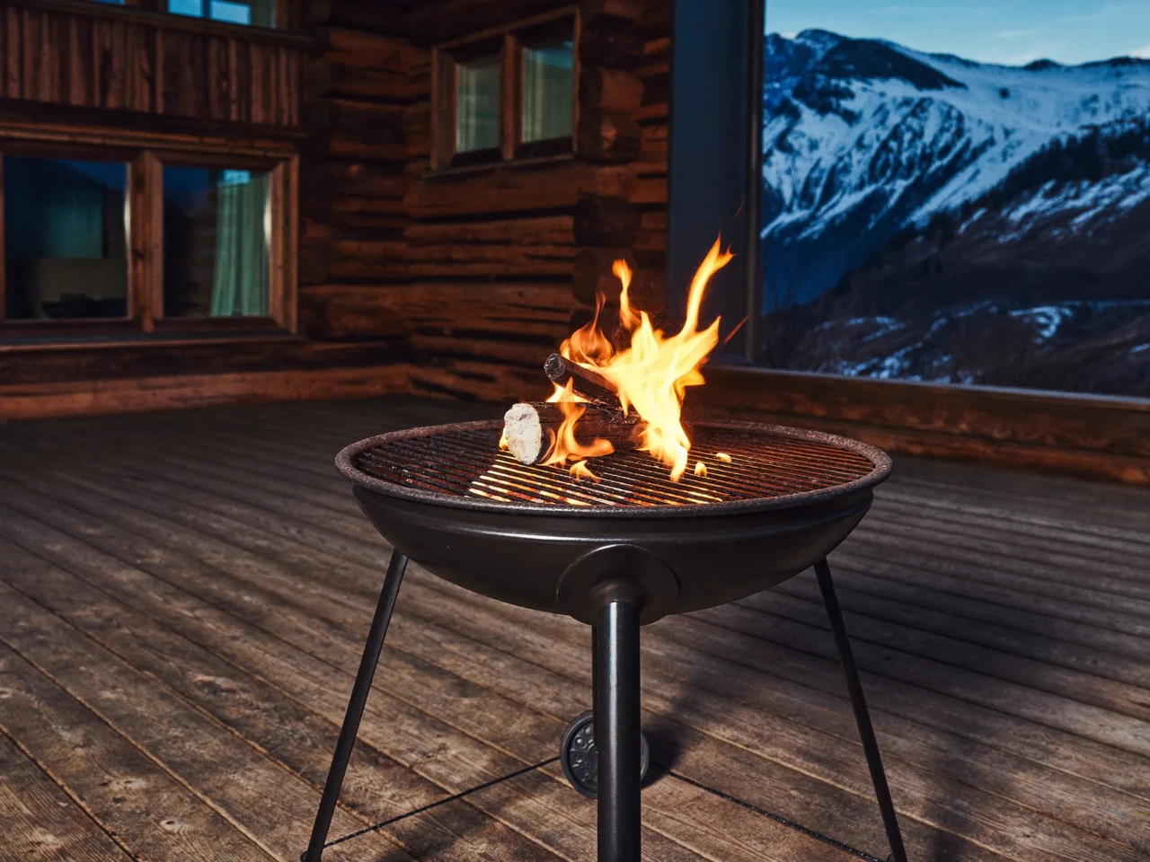 Illustration: Holzkohlegrill auf einer Terrasse im Abendlicht vor einem Chalet in den Alpen
