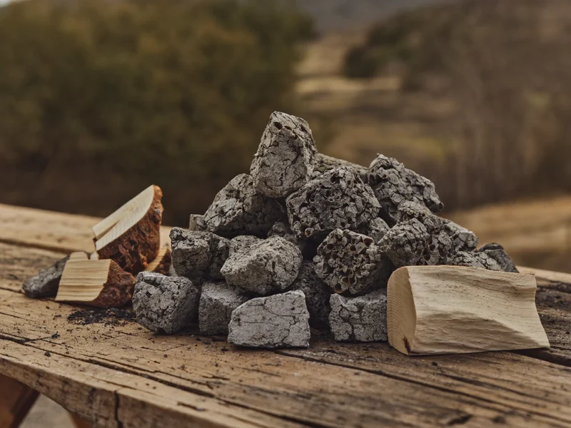 Illustration: Stücke Holzkohle neben gespaltenem Buchenholz auf einer rustikalen Werkbank